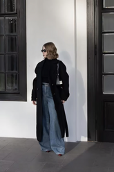 a lady in a black sweater, a long black wool coat and a pair of wide leg jeans